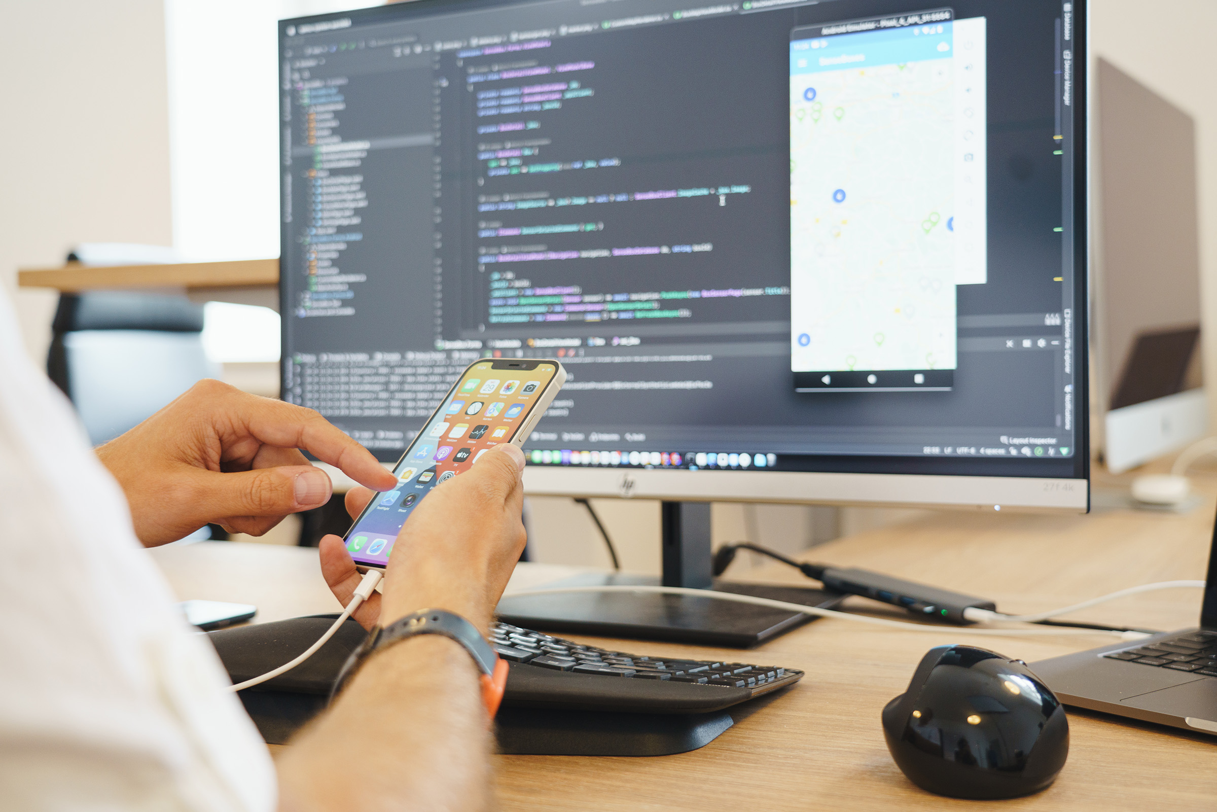 Entwickler testet mobile App auf Smartphone während der App-Programmierung am Desktop – Beispiel für App-Entwicklung und UI/UX-Design bei Cayas.
